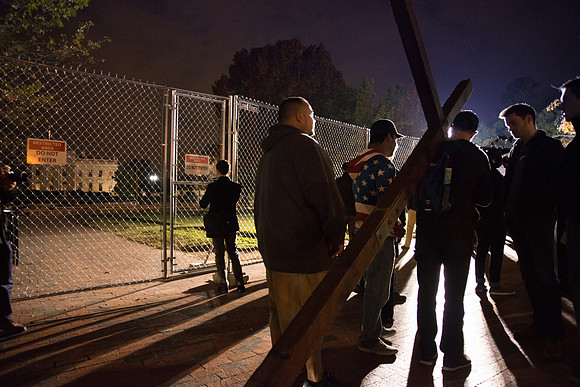 Man with cross talking to people outside of The White House  on